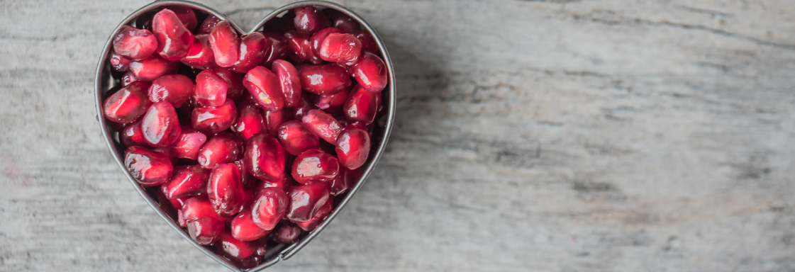 Fotografía de un plato con forma de corazón, lleno de granos de granada, sobre una mesa gris. Foto por Jessica Lewis para Pexels