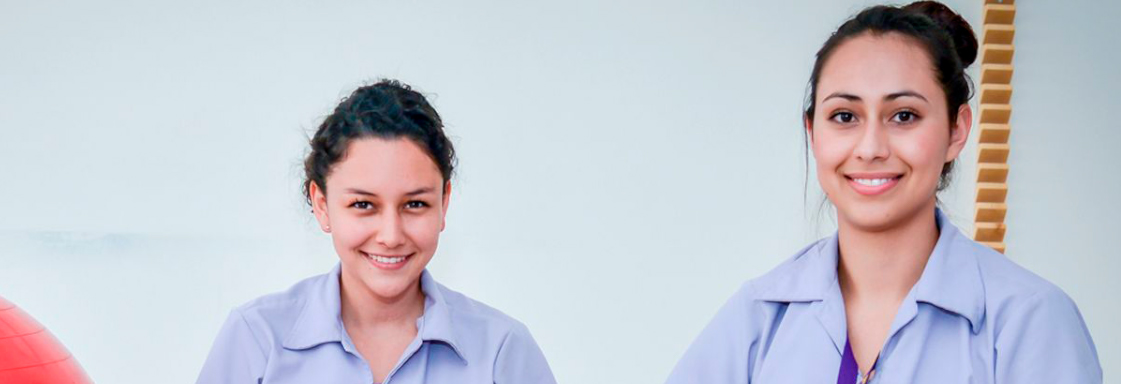Dos alumnas, con el uniforme color púrpura de la Universidad Teletón, sonríen a la cámara en un espacio abierto con fondo blanco