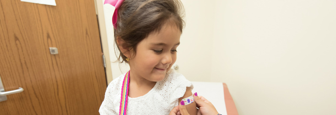 Fotografía de niña sonriente recibiendo una vacuna en un consultorio. Foto por la CDC para Unsplash.