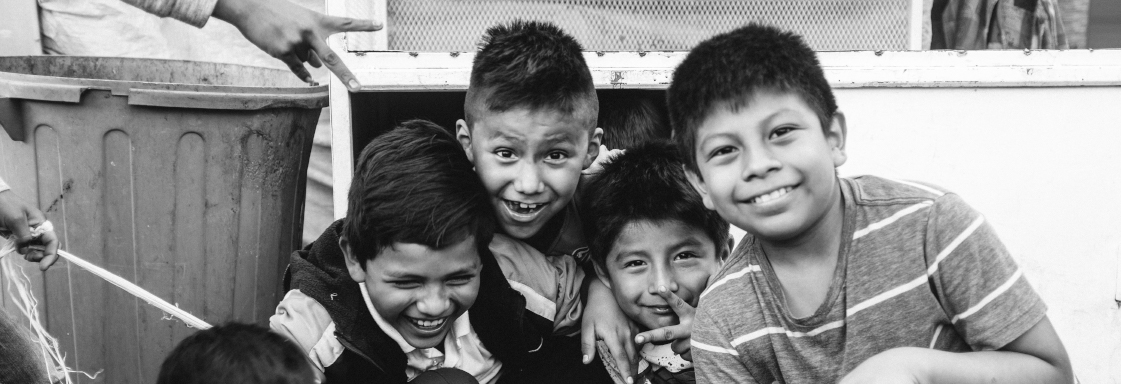Fotografía en blanco y negro de un grupo de niños mexicanos. Son cinco. Están sonriendo a la cámara.